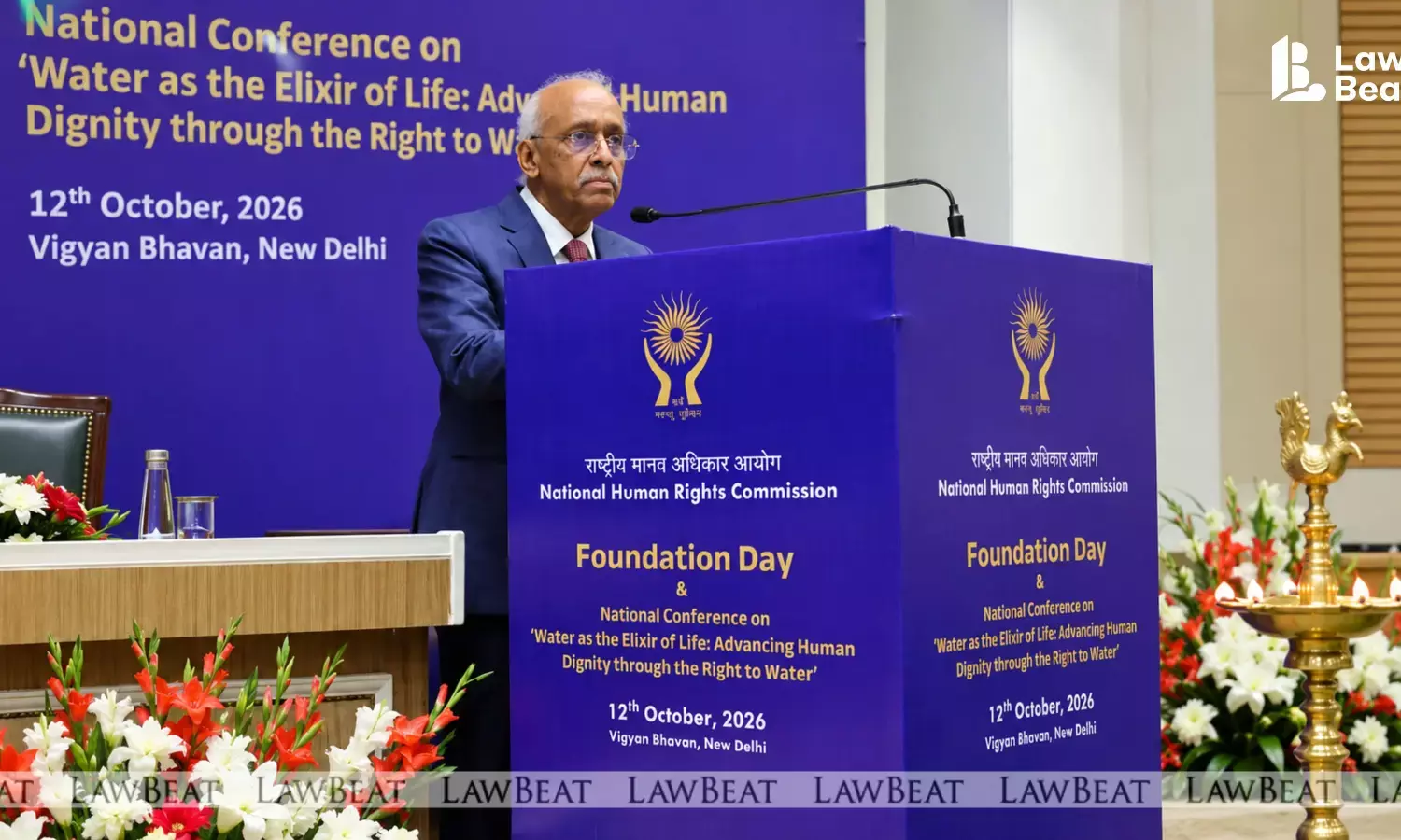 Justice V. Ramasubramanian, Chairperson of the National Human Rights Commission, speaking at a podium at the NHRC Foundation Day event, with Chief Justice of India Surya Kant seated on the dais.